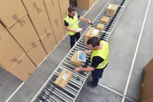 Two men in high vis jackets are scanning parcels on a conveyor in a warehouse as part of the intake, despatch or returns process