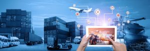 A person holds a tablet bursting with information against a blue background featuring different modes of freight including a docked container vessel, dozens of stacked containers and HGVs in the port as a cargo plane flies above